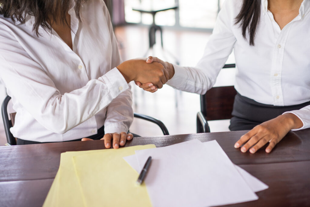 closeup of two business women shaking hands and sitting at desk